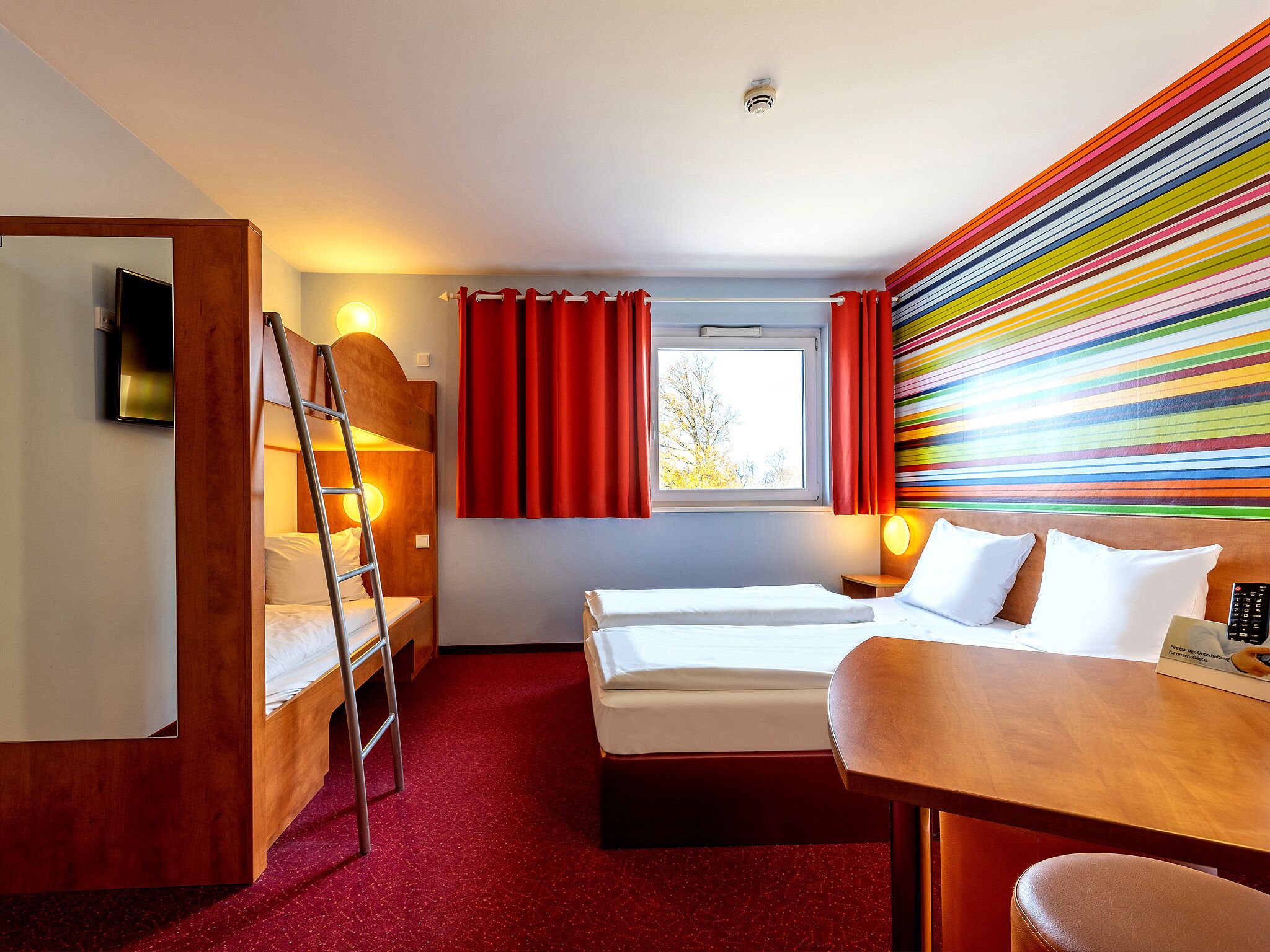 Una habitación de hotel con literas, un escritorio y una pared colorida a rayas.
