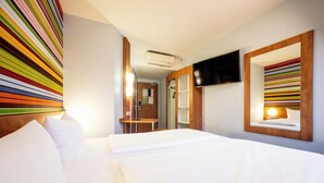 A hotel room with a bed, a TV mounted on the wall, and a striped wall decoration.