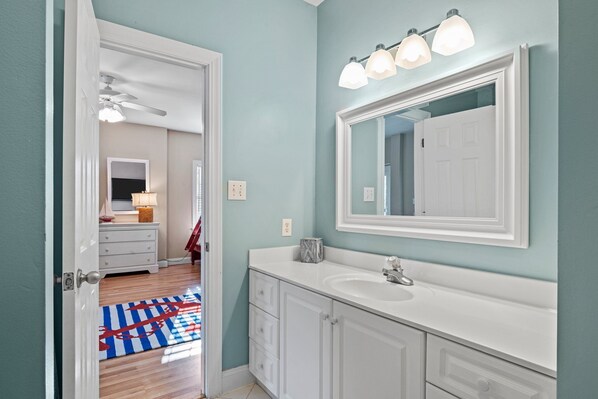 A bathroom with a white vanity, a large mirror, and a ceiling fan.
