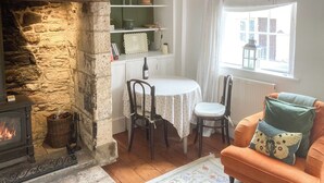 Una sala de estar acogedora con chimenea de piedra, una mesa de comedor con sillas y un ventanal con vistas a edificios.