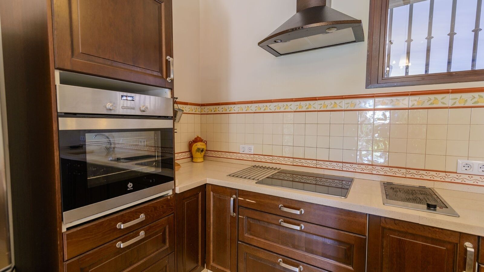 Eine Küche mit Holzausstattung, einem Backofen, einer Mikrowelle und einem Fenster mit Gitterstäben.