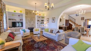 A spacious living room with white sofas, a coffee table, and a fireplace. There are shelves with books and decorative items, and a staircase leading to another level. - Cortijo Escondido Arcos de la Frontera by Ruralidays (Cádiz)