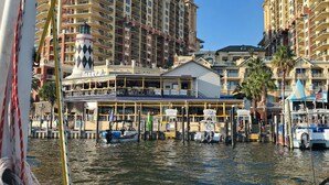 A marina with boats docked, a building with a lighthouse, and a hotel with balconies. -  Luxury home with sugar white sand beach, family-friendly vacation rental house! (Destin)