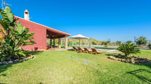A red building with a covered patio area, outdoor seating with lounge chairs, and a clear blue sky.
