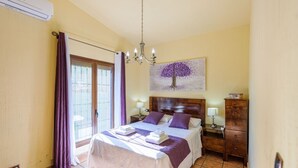 Un dormitorio con cama, mesita de noche, cómoda, candelabro y un cuadro de un árbol.