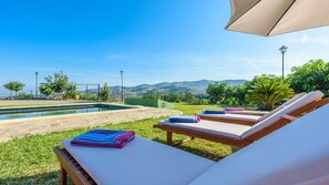 A poolside area with lounge chairs and towels, a clear view of mountains, and a well-maintained lawn.
