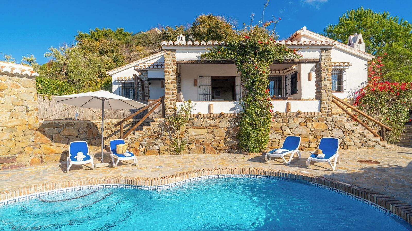 Un espace aménagé au bord de la piscine, avec un mur en pierre, une piscine et trois chaises longues.