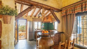 A rustic kitchen with a large pot on the stove, wooden beams, and a view of the outdoors.