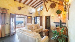 A cozy living room with a leather sofa, a wooden coffee table, and a view of the sea through an open door.