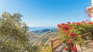 A scenic view from a stone staircase with a wooden railing, overlooking a coastal landscape with hills and the sea.