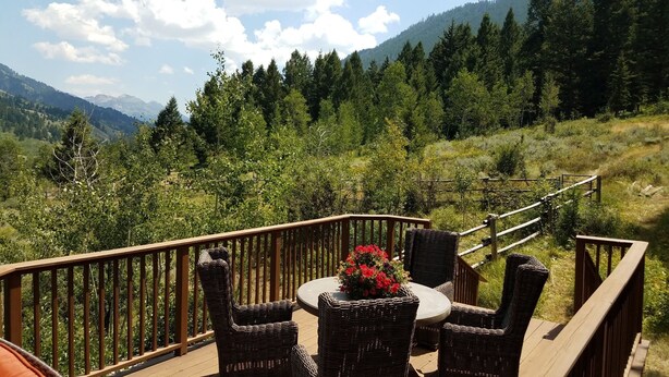A deck with wicker furniture and a table, overlooking a forested hillside. - Teton Views & Privacy in Jackson Home - 30 day minimum rentals (Jackson)