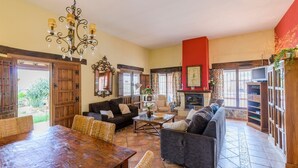 A spacious living room with a fireplace, wooden furniture, and a large dining table. - El Pino de Sayalonga by Ruralidays (Málaga)