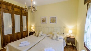 A double bed with two nightstands, a chandelier, and two framed artworks on the wall. - El Pino de Sayalonga by Ruralidays (Málaga)