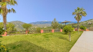 A grassy outdoor area with a stone pathway, a palm tree, and a mountain view. - El Pino de Sayalonga by Ruralidays (Málaga)