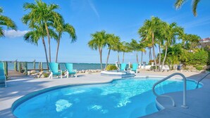 A swimming pool with a curved edge, surrounded by palm trees and beach chairs, with a view of the ocean. - Ocean's Paradise is an exquisite 4-bedroom, 3-bathroom retreat nestled within the sought-after enclave of Sombrero Beach (Marathon)