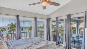 A bedroom with a large bed, a ceiling fan, and a view of the ocean. - Ocean's Paradise is an exquisite 4-bedroom, 3-bathroom retreat nestled within the sought-after enclave of Sombrero Beach (Marathon)