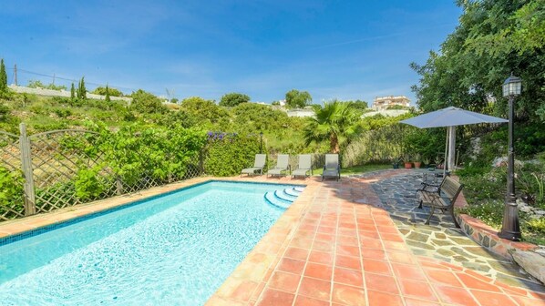 A rectangular swimming pool with a tiled edge, surrounded by a stone patio. There are lounge chairs and a bench along the patio, and a lamp post is visible. - La Haza de Frigiliana by Ruralidays (Málaga)