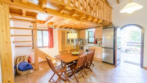 Een houten eethoek met een tafel en stoelen, een keuken met kasten en apparatuur, en uitzicht op buiten.