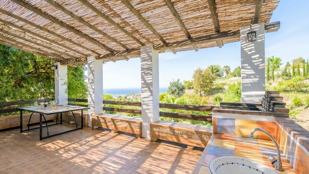 Een terras buiten met een tafel, banken, een barbecue en uitzicht op het landschap.