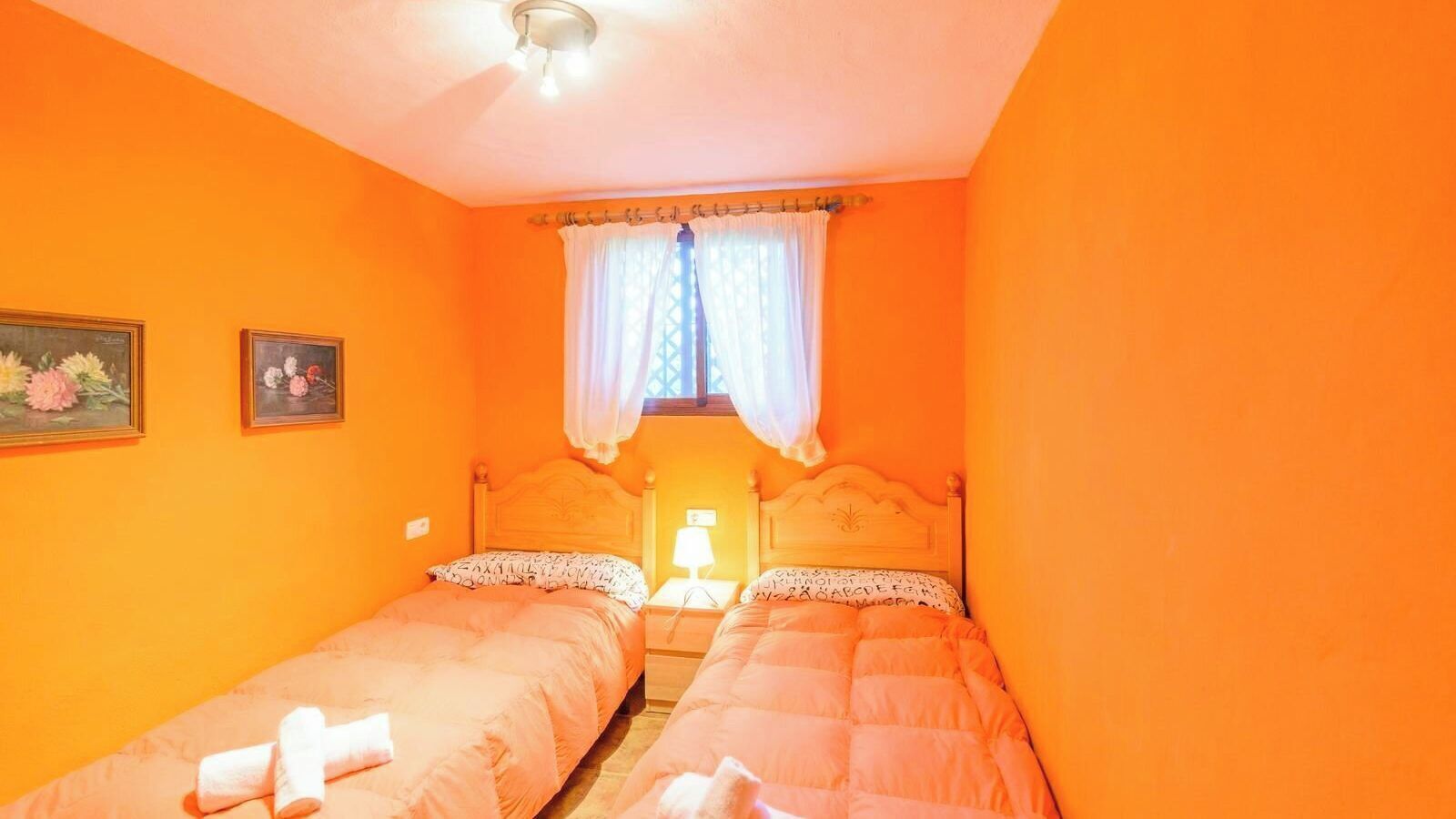 A room with two beds, a nightstand with a lamp, and a window with a curtain.