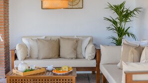 Een gezellige zithoek met een bank, een bijzettafeltje met een schaal fruit en een theepot, en een bloempot met een plant.
