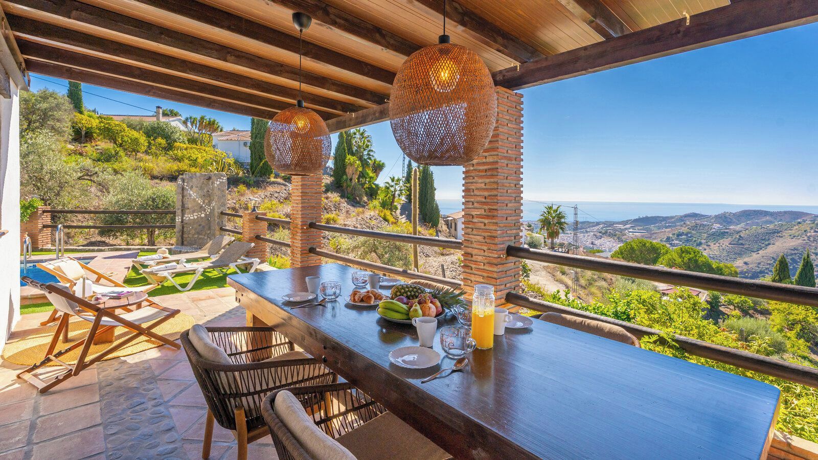 An outdoor dining area with a view of the countryside, a pool, and lounge chairs.