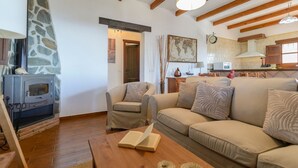 Een gezellige woonkamer met een stenen openhaard, een bank, een fauteuil en een houten salontafel.