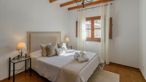 Een slaapkamer met een bed, twee nachtkastjes, een raam met gordijnen en een houten plafondbalk.