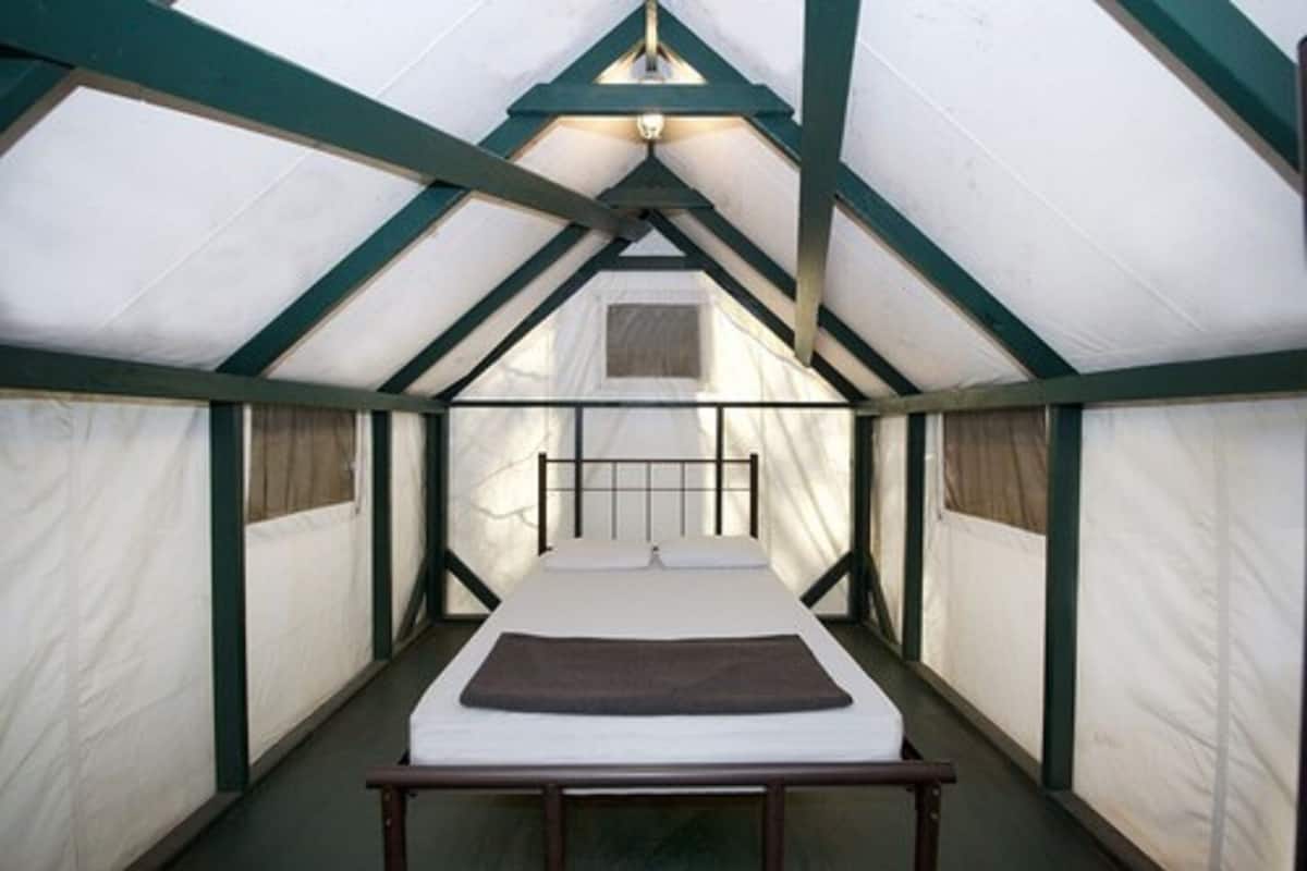 A tent with a single bed, a window, and a light fixture.