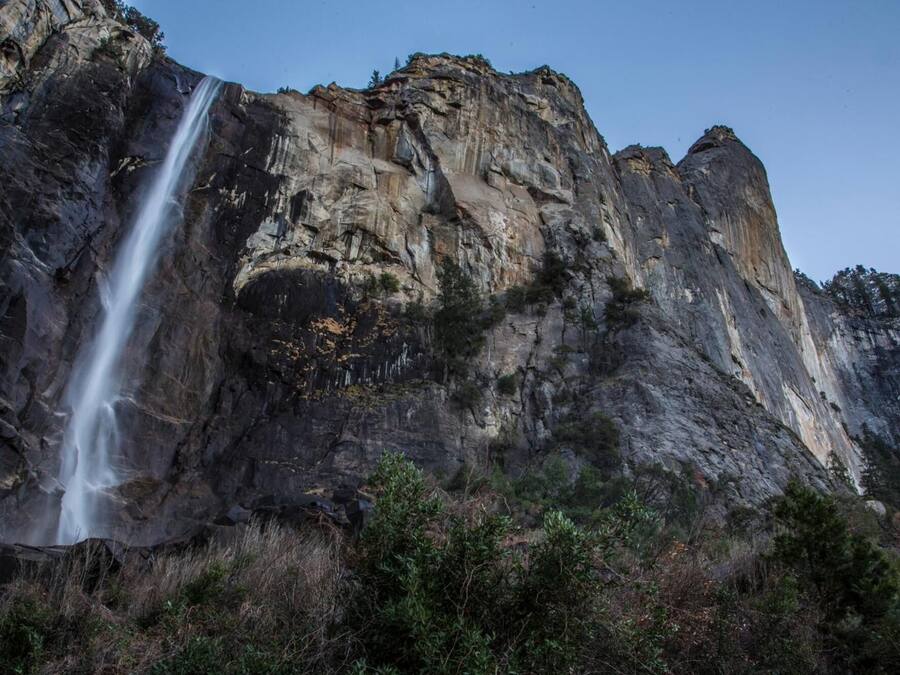 A waterfall cascading down a rugged cliff face with dense vegetation at the base.