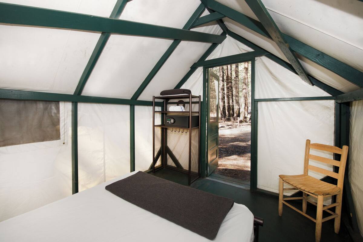 A tent with a bed, a chair, and a small table with a device.
