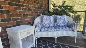 A white wicker sofa with floral cushions, a matching side table, and a black and white patterned rug on a wooden deck. - Island getaway near farmland, a bird sanctuary, nature walks, & close  to beach (Comerong Island)
