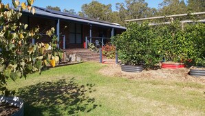 A house with a covered porch, a brick exterior, and a lawn with potted plants. - Island getaway near farmland, a bird sanctuary, nature walks, & close  to beach (Comerong Island)