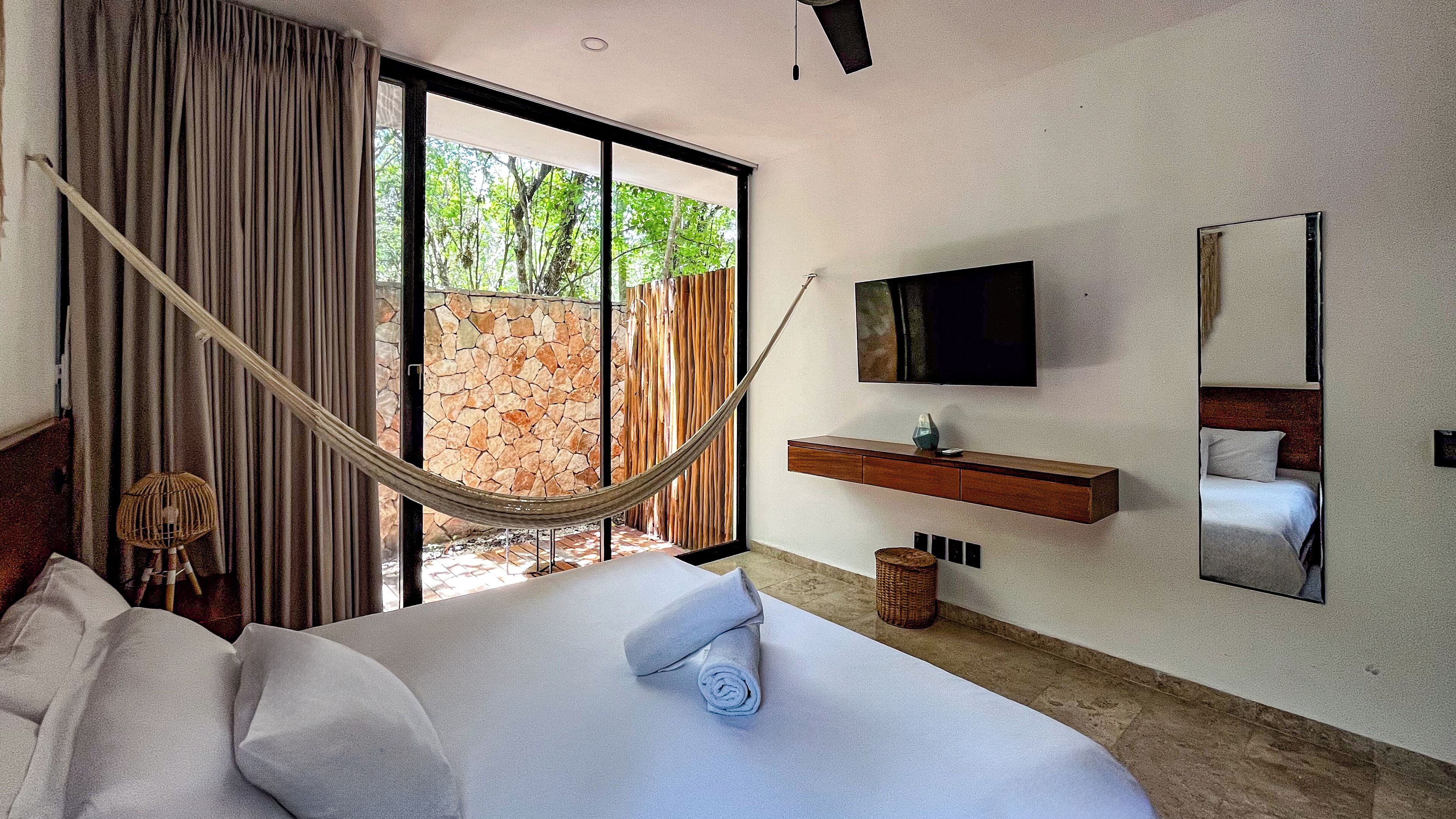 Habitació d'hotel moderna amb un llit gran, una cadira d'hamaca, una televisió i vistes a la vegetació.