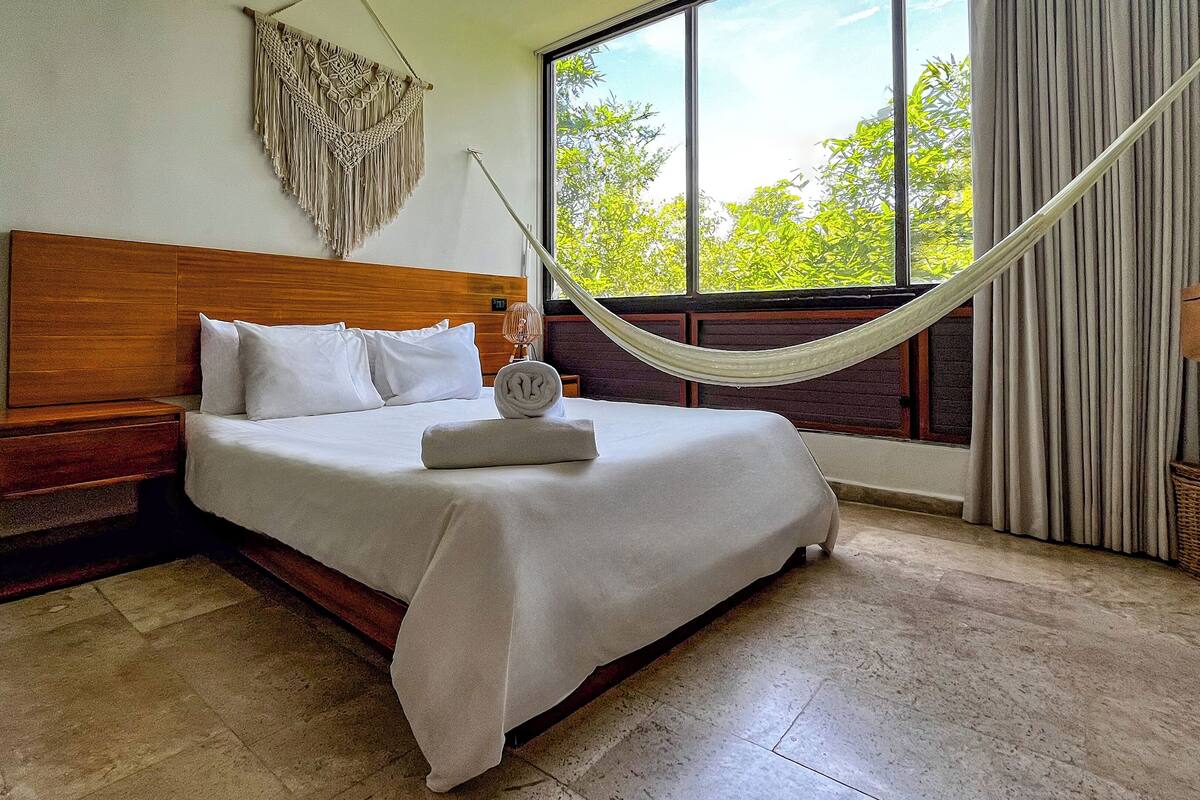 Un lit bien fait, avec du linge de lit blanc, une tête de lit en bois et une décoration murale en macramé.