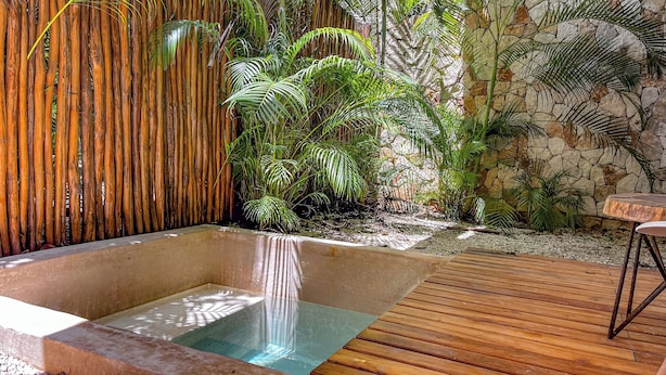 Un jacuzzi con caída de agua, rodeado de exuberante follaje y un muro de piedra.