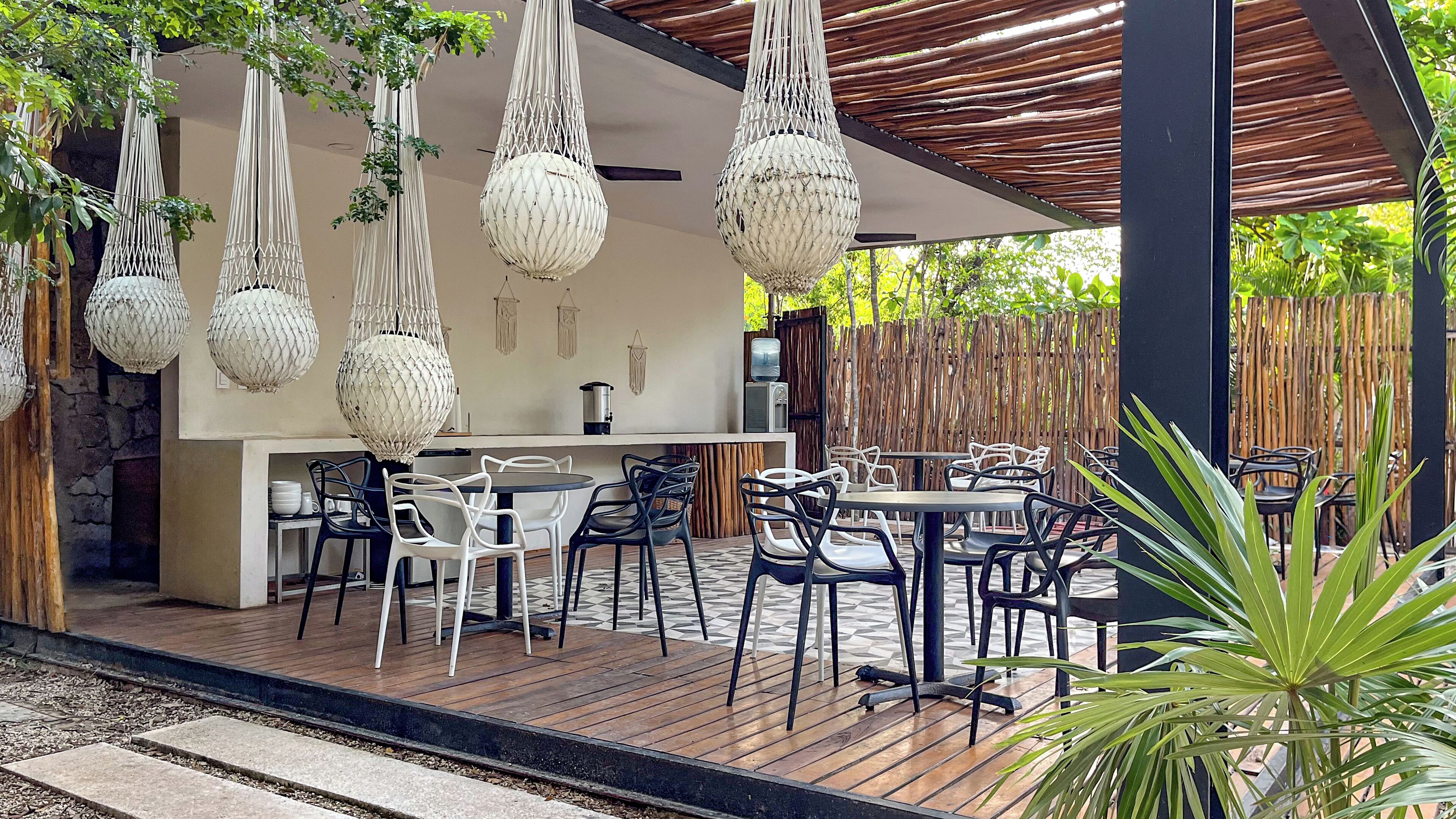 An outdoor patio with a wooden deck, white and black chairs, a bar area with a white countertop, and hanging macramé light fixtures.