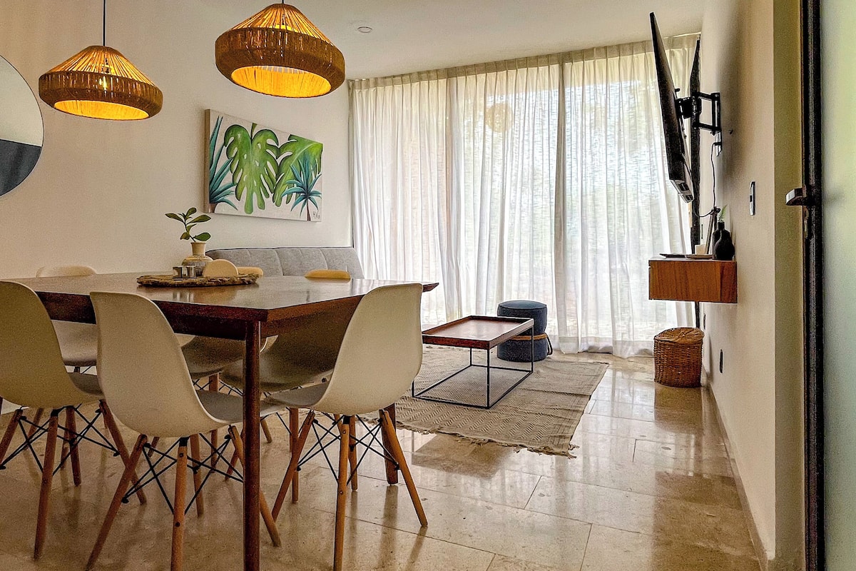 Un espace repas avec une table en bois, des chaises blanches et des luminaires suspendus.