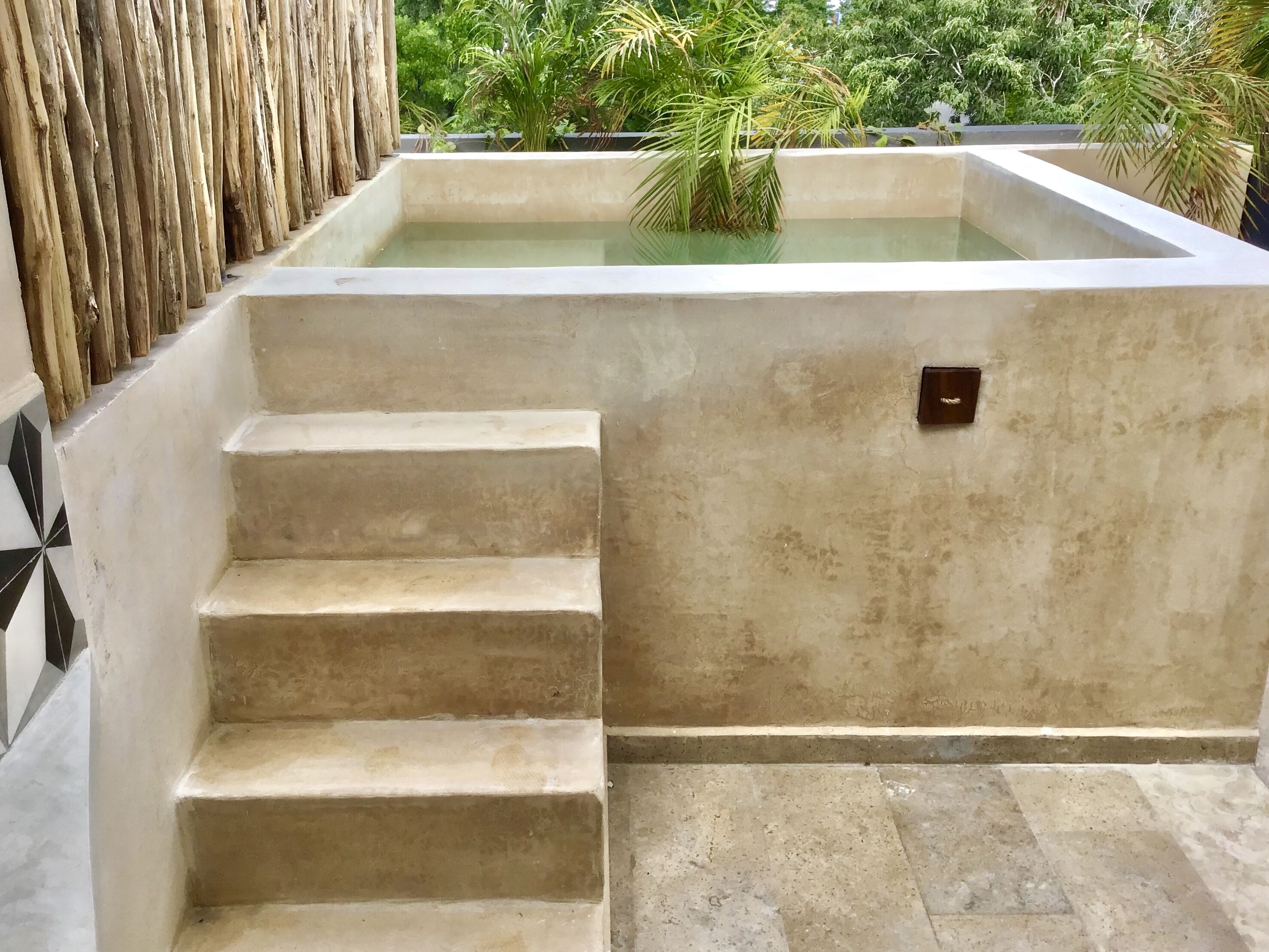 A concrete staircase leading to a pool area with a textured wall and a small electrical outlet.