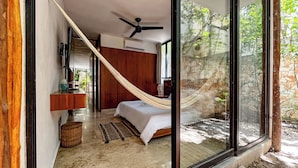Un dormitorio con cama, hamaca, ventilador de techo, pared de piedra y un ventanal grande.