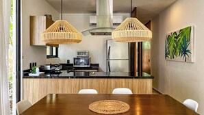 Una cocina moderna con una isla de madera, dos lámparas colgantes de mimbre y un refrigerador de acero inoxidable, además de un cuadro en la pared.