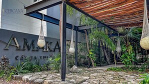 Un edificio moderno con un letrero que dice 'AMAKA PROPERTY MANAGEMENT' y un espacio exterior cubierto con macetas colgantes y vegetación.