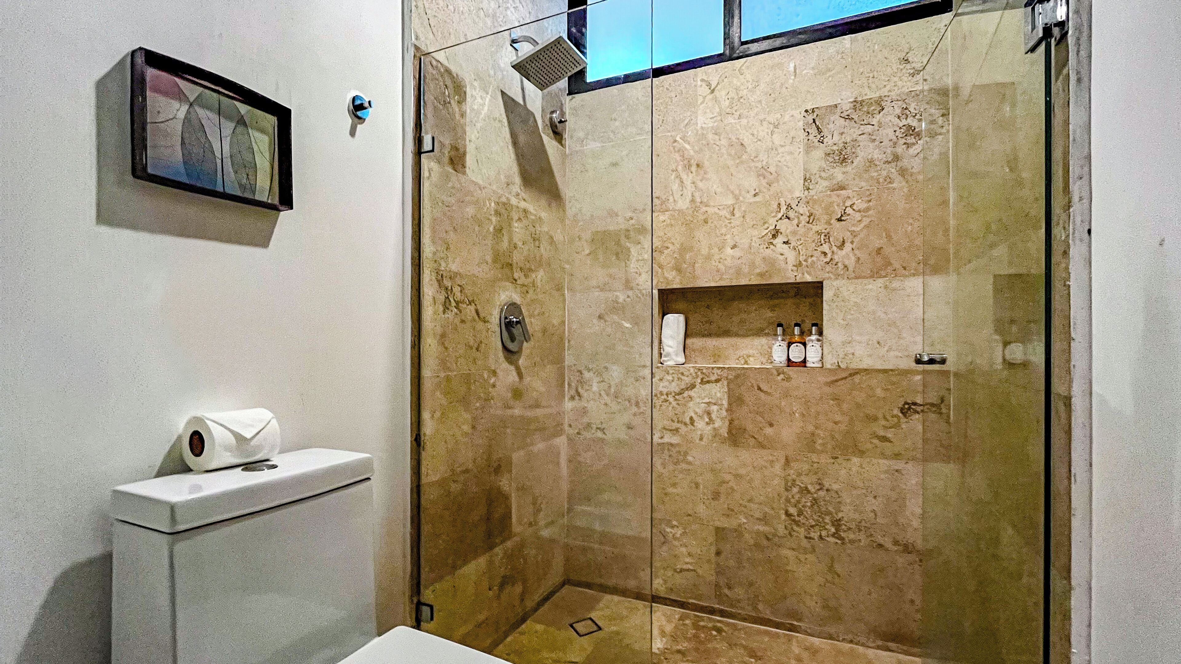 Un baño moderno con ducha de vidrio, inodoro, lavamanos y un estante pequeño con artículos de tocador.