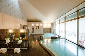 A modern indoor swimming pool with a view of the city, a sauna area, and a tiled wall with a geometric pattern. - Kamenoi Hotel Kanonji (Kanonji)