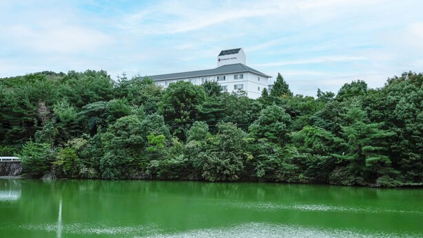 A building surrounded by dense greenery, likely a hotel, with a calm body of water in the foreground. - Kamenoi Hotel Kanonji (Kanonji)