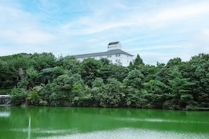 A building surrounded by dense greenery, likely a hotel, with a calm body of water in the foreground. - Kamenoi Hotel Kanonji (Kanonji)