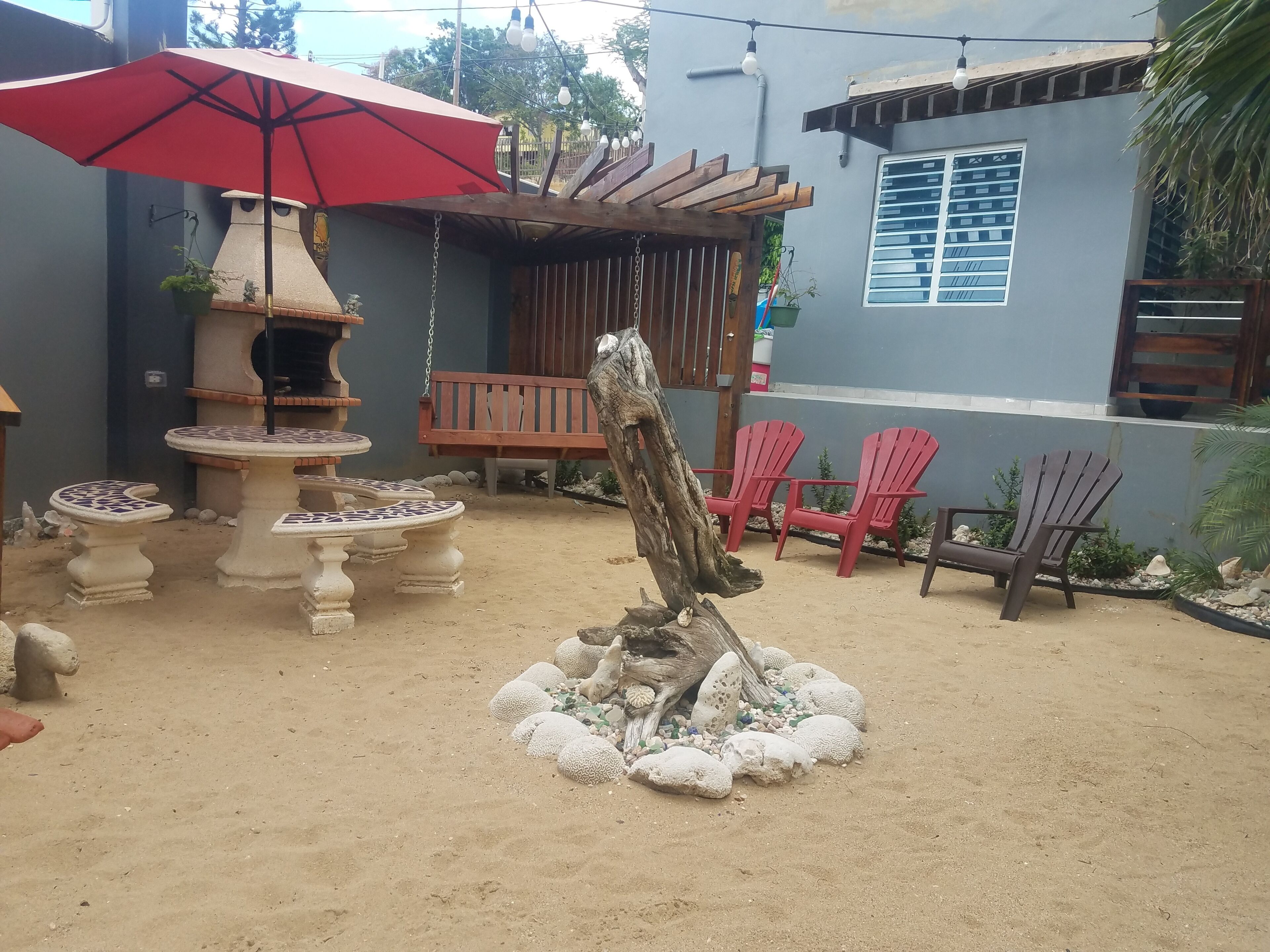 A patio area with a red umbrella, outdoor seating, a wooden pergola, and a decorative stone arrangement.