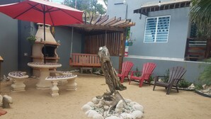A patio area with a red umbrella, outdoor seating, a wooden pergola, and a decorative stone arrangement. - Caribbean getaway aguadilla (Aguadilla Pueblo)
