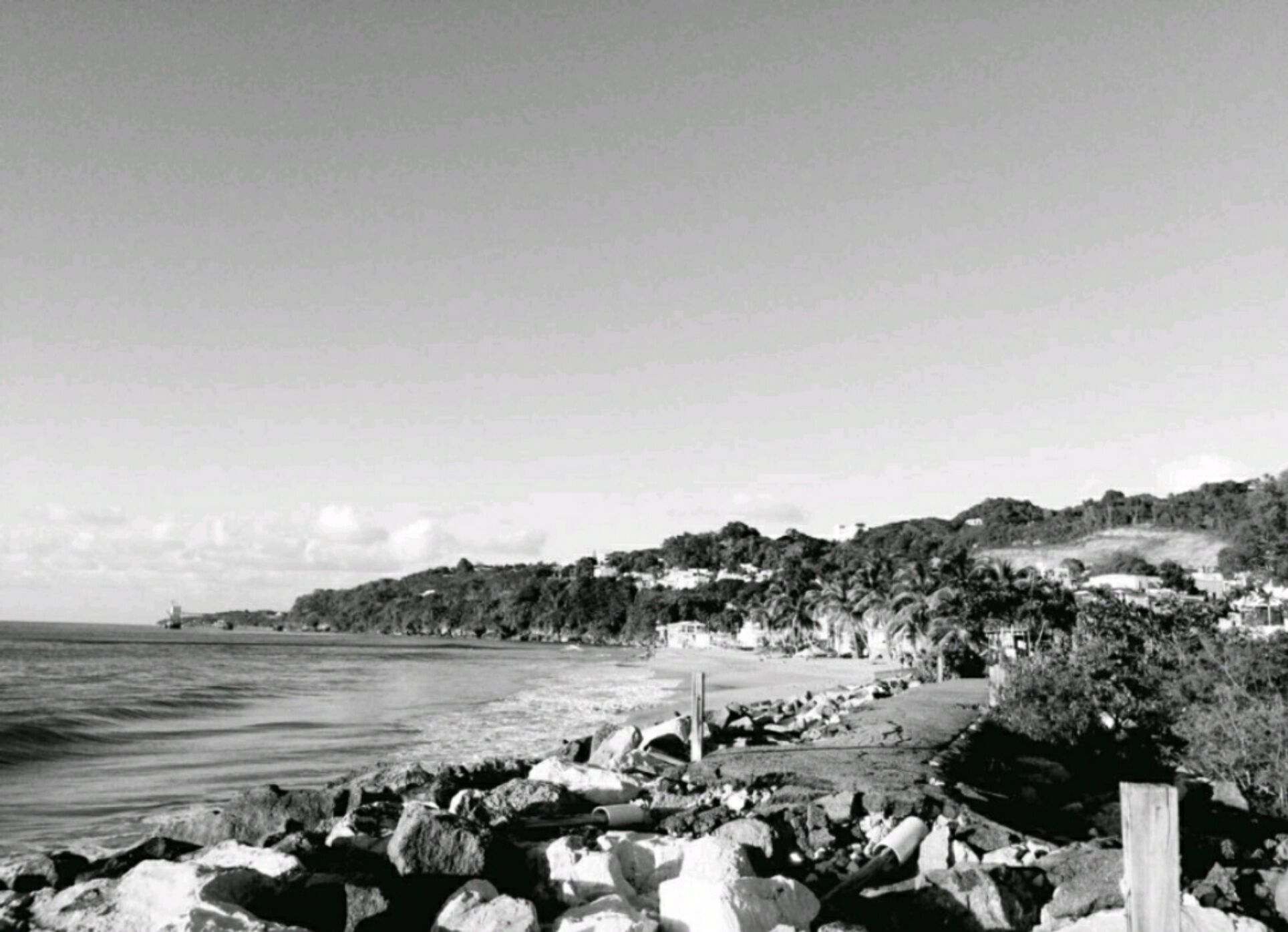 A coastal landscape with rocky shoreline, a lighthouse, and a hill with buildings.