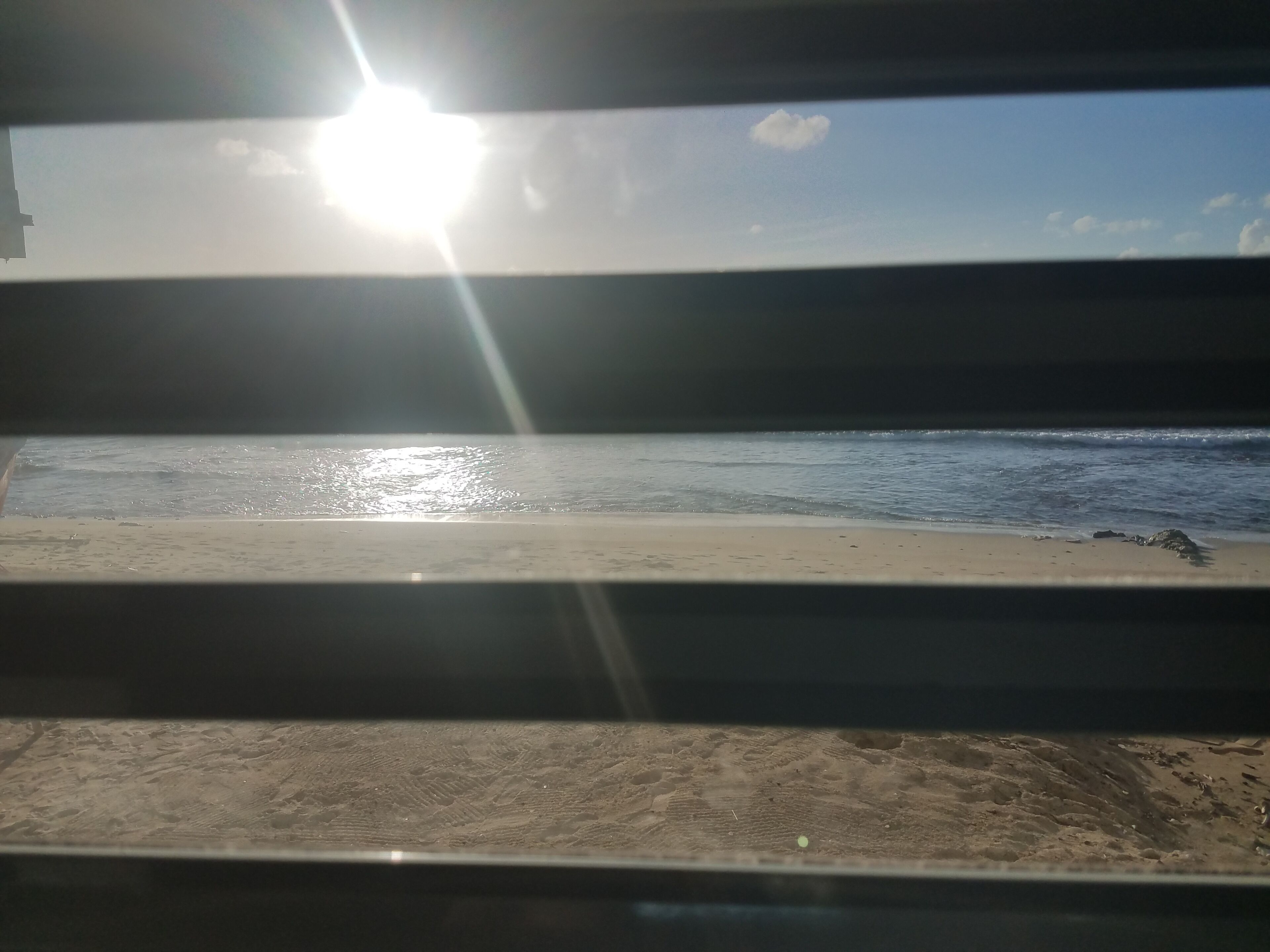 A beach view through a window with sunlight reflecting off the water.